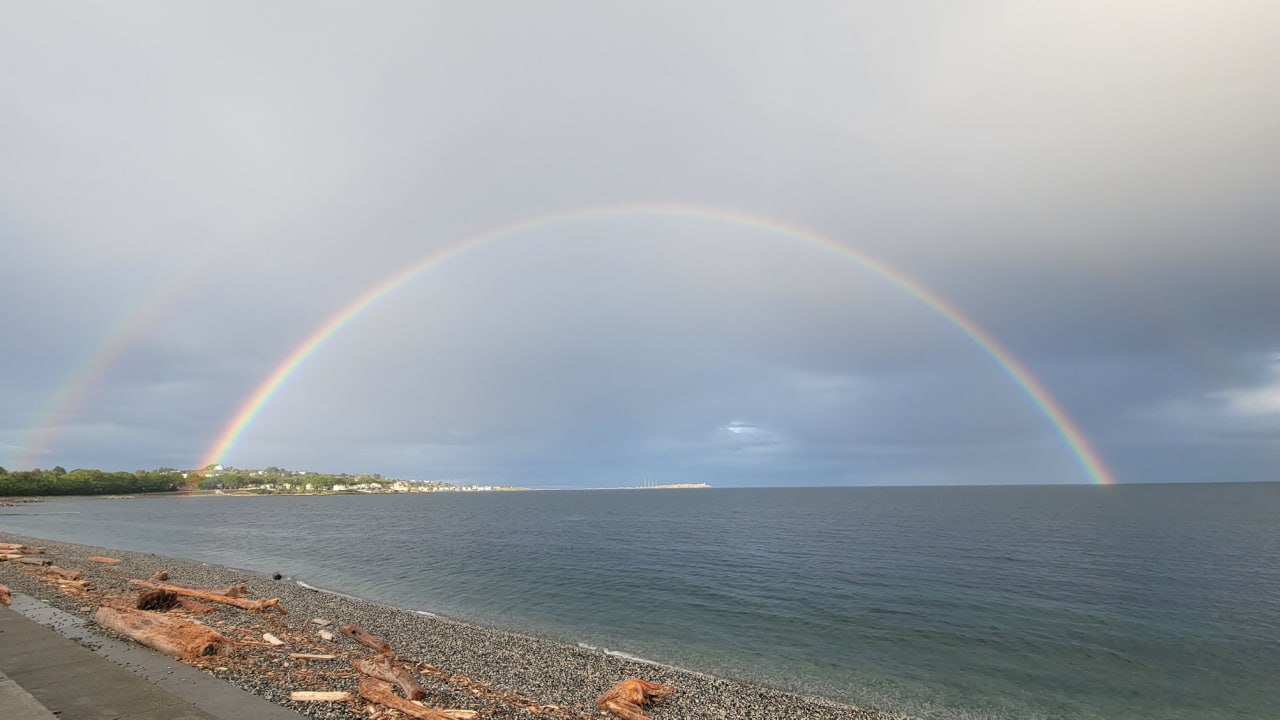 Double rainbow over a pebble beach and calm coastal water